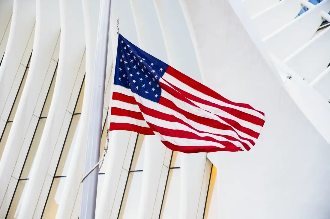 Bandeira dos Estados Unidos hasteada diante de uma arquitetura moderna de vidro e a&ccedil;o.